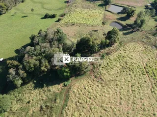 Vista aérea de uma área rural com campos gramados e vegetação densa.