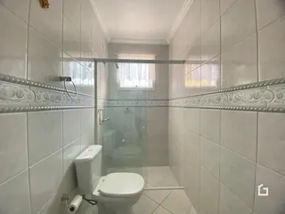 Foto de um banheiro com revestimento cerâmico e box de vidro.