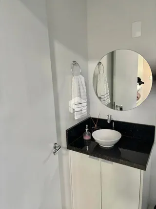 Foto de um banheiro com bancada escura e armários brancos.