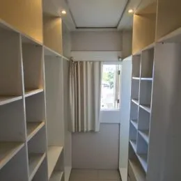 Corredor interno com prateleiras brancas e cortinas claras.