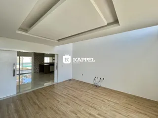 Ambiente interno de uma sala com piso de madeira clara e teto alto.