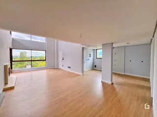 Uma sala de estar ampla com piso de madeira clara e grandes janelas.
