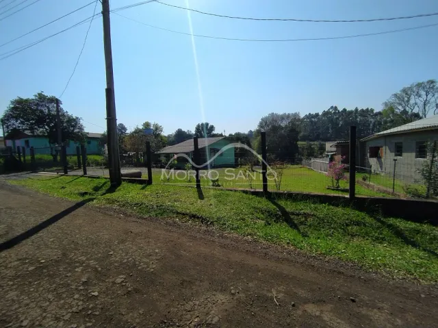 Vista externa de um terreno com grama e árvores sob um céu azul.