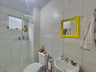 Interior de um banheiro com revestimento cerâmico branco e box de vidro.