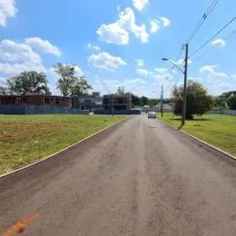 Vista externa de uma rua asfaltada com grama nas laterais sob um céu azul.