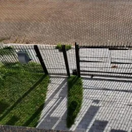 Vista externa de um pátio pavimentado com grade metálica.