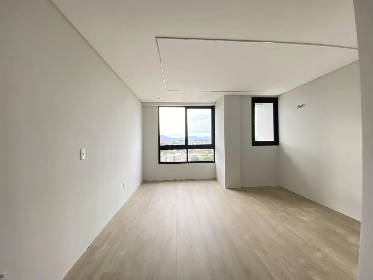 Sala de estar ampla com piso de madeira e janela com vista da paisagem urbana.