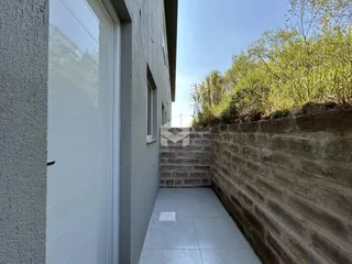 Vista lateral da fachada de uma residência com muro de tijolos e piso externo.