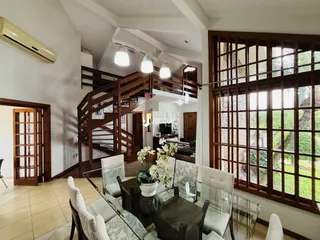 Sala de jantar iluminada com grandes janelas e escadaria de madeira.