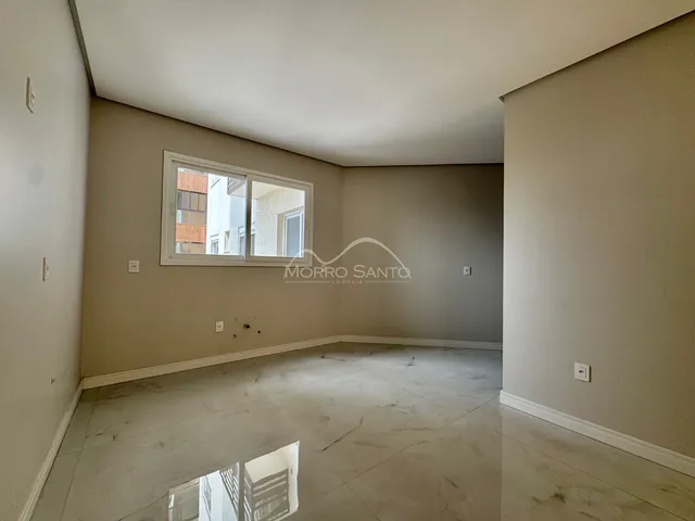 Uma sala ampla e vazia com piso claro e janela.
