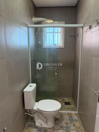 Interior de um banheiro com box de vidro e vaso sanitário branco.