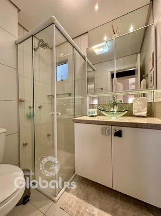 Foto de um banheiro com box de vidro e louças brancas.