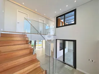 Vista do interior de uma sala com escadaria de madeira e guarda-corpo de vidro.