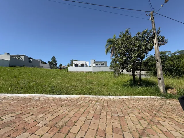 Vista externa mostrando uma área pavimentada e um campo gramado em frente a edifícios residenciais.