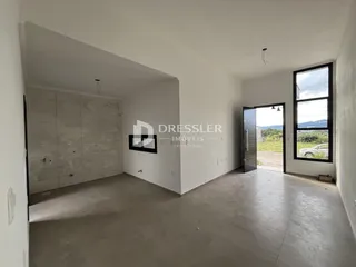 Ambiente interno de uma sala ampla com paredes brancas e piso claro.