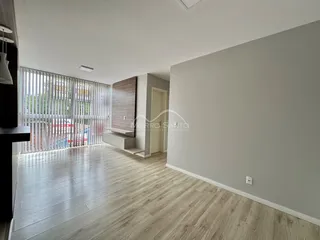 Sala de estar com piso de madeira clara e janela com persianas.