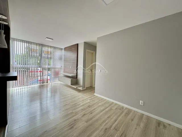 Sala de estar com piso de madeira clara e janela com persianas.