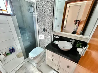 Foto interna de um banheiro com box de vidro e bancada escura.