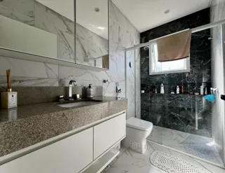 Banheiro com bancada de granito e box de vidro transparente.