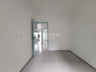 Corredor interno de uma residência com paredes brancas e piso de cerâmica clara.