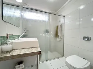 Banheiro com bancada de pedra e box de vidro transparente.