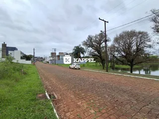 Vista da rua de paralelepípedos em Lajeado, Brasil, com vegetação e um corpo d'água ao lado.