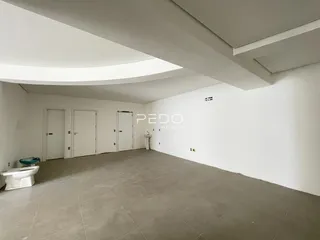 Interior de uma sala ampla com paredes brancas e piso de concreto.