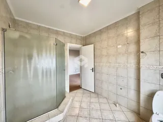 Interior de um banheiro com revestimento cerâmico e box de vidro.