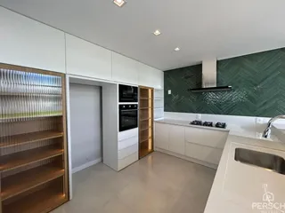 Vista da cozinha moderna com armários brancos e revestimento verde na parede.