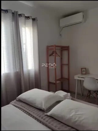 Quarto com duas camas e janela com cortinas claras.