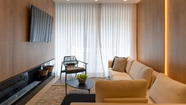 Sala de estar com cortinas brancas e sofá claro.