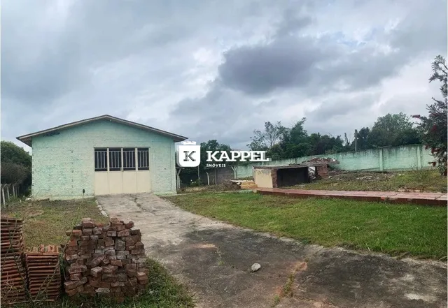Fachada externa de uma edificação com revestimento verde claro e acesso por uma estrada de terra.