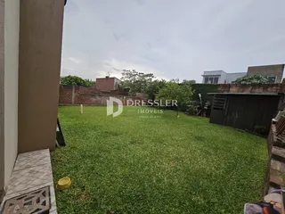 Vista externa de um quintal gramado com muro de tijolos e estrutura de madeira.