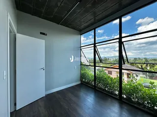 Vista interna de uma sala com piso de madeira escura e grande janela com vista para a paisagem.