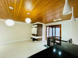 Interior de uma sala de estar com teto de madeira e cozinha em um imóvel no Brasil.