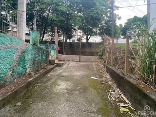 Vista externa de um pátio com cerca e vegetação ao lado de um muro.