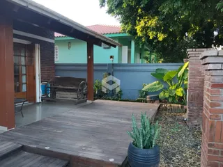 Fachada de uma residência com deck de madeira e vegetação no quintal.