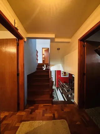 Vista de um corredor com escadaria de madeira em uma residência.