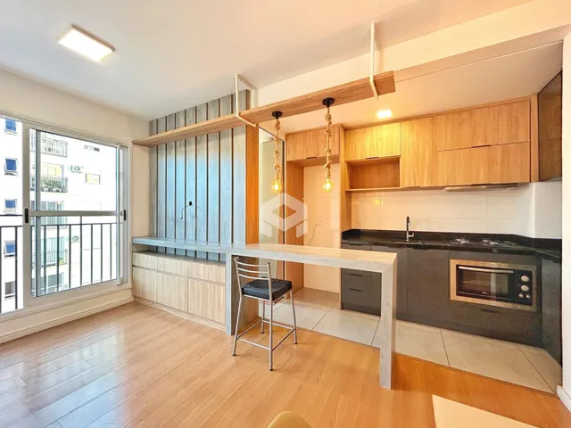 Sala de estar e cozinha com piso de madeira clara e armários modernos.