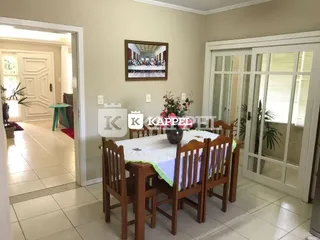 Uma mesa de jantar de madeira com cadeiras está posicionada em um ambiente interno.