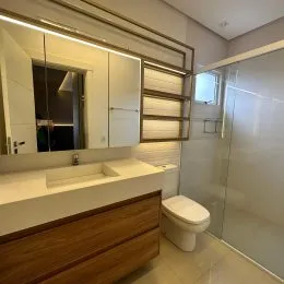 Foto de um banheiro com bancada branca e box de vidro transparente.