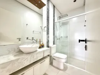Banheiro moderno com bancada de mármore e box de vidro.