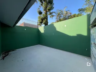Vista de um pátio externo com parede verde e piso de concreto.