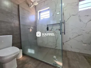 Banheiro com box de vidro e revestimento de azulejos brancos.