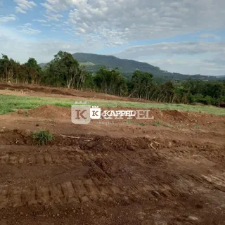 Foto de um terreno aberto com solo marrom e vegetação rasteira em uma área rural.