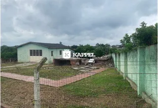 Vista externa de uma propriedade com um terreno gramado e cerca verde.