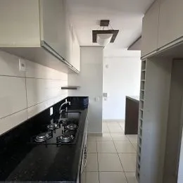 Detalhe da bancada escura e armários brancos de uma cozinha.