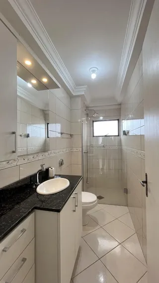 Banheiro com revestimento de azulejos brancos e bancada escura.