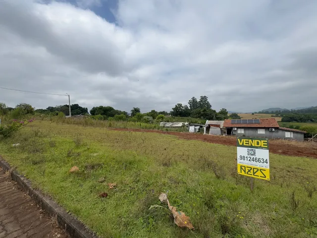 Vista externa de uma propriedade rural com campo gramado e sinal de venda.
