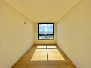 Vista interna de um ambiente com piso de madeira e janela para a paisagem urbana.